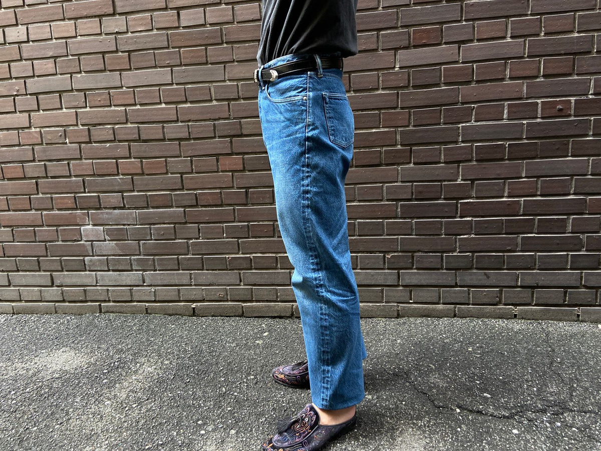 A pair of washed jeans seen from the side, showing the waist position and the line to the hem