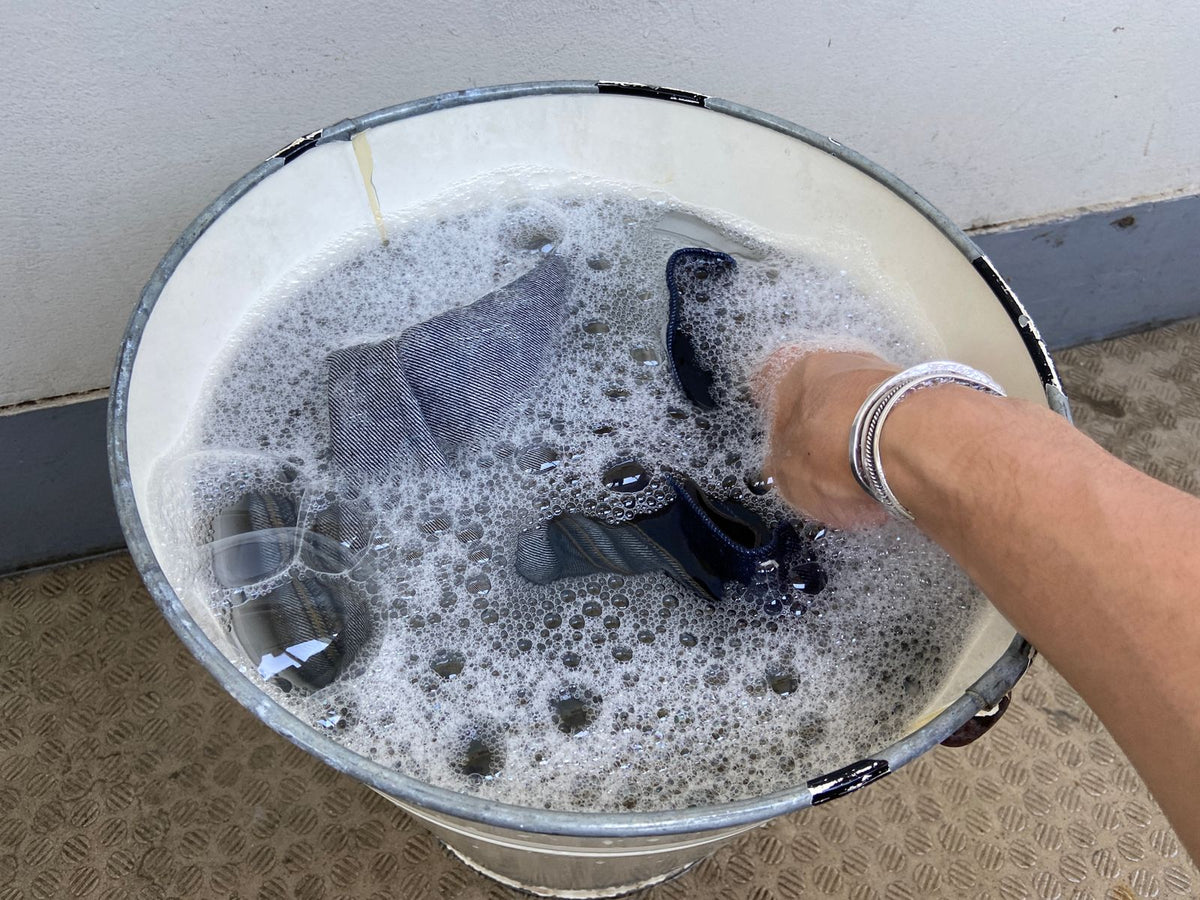 Denim turned inside out being worked by hand in a bucket of detergent solution