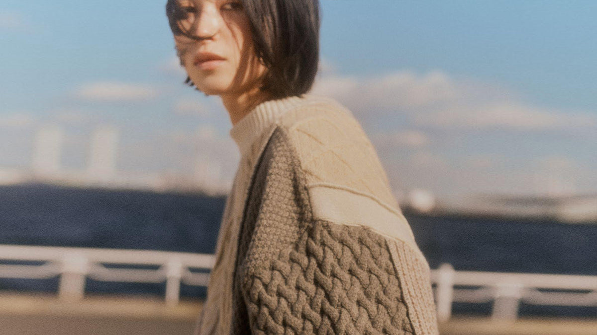 A model in a cable knit panelled in ecru and greige against a seaside sky