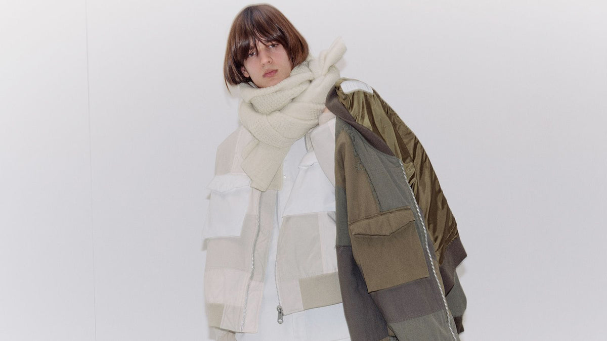 A model in an ecru scarf and a patchwork khaki blouson against white