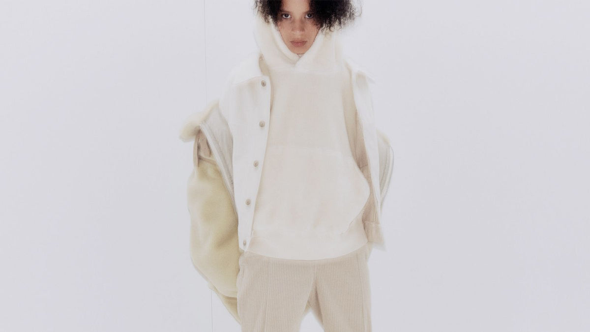 A model in an ecru hooded sweat under a shearling vest against white