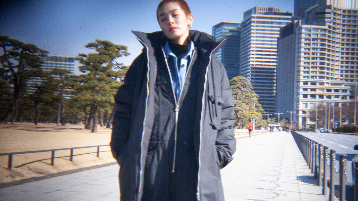 A model in a navy long down coat with the collar up, on a winter Tokyo promenade