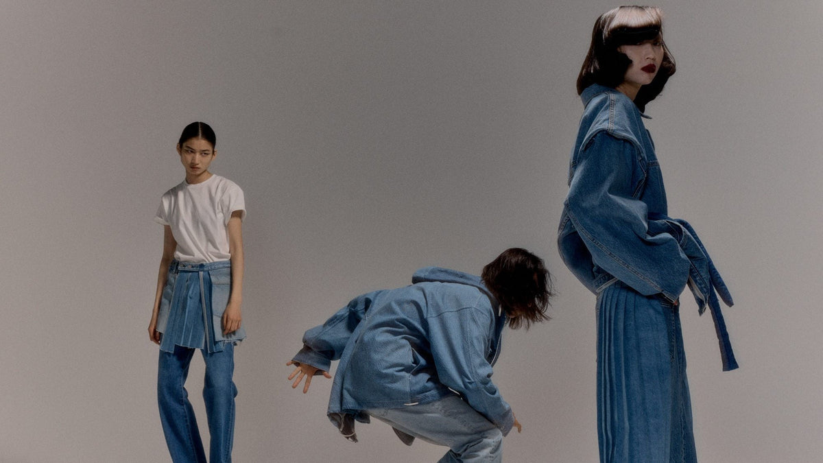 Studio shot of three looks side by side: a white tee with a denim wrap skirt over jeans, a denim jacket worn bending forward, and a denim jacket with a long pleated denim skirt.